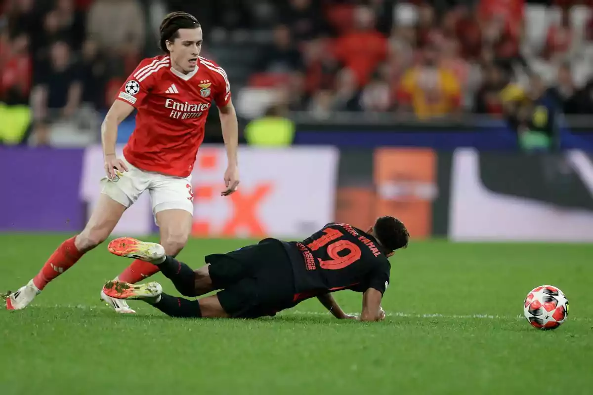 Un jugador de Benfica disputa el balón mientras un rival de camiseta negra cae al césped durante un partido de fútbol Un jugador de Benfica disputa el balón mientras un rival de camiseta negra cae al césped durante un partido de fútbol