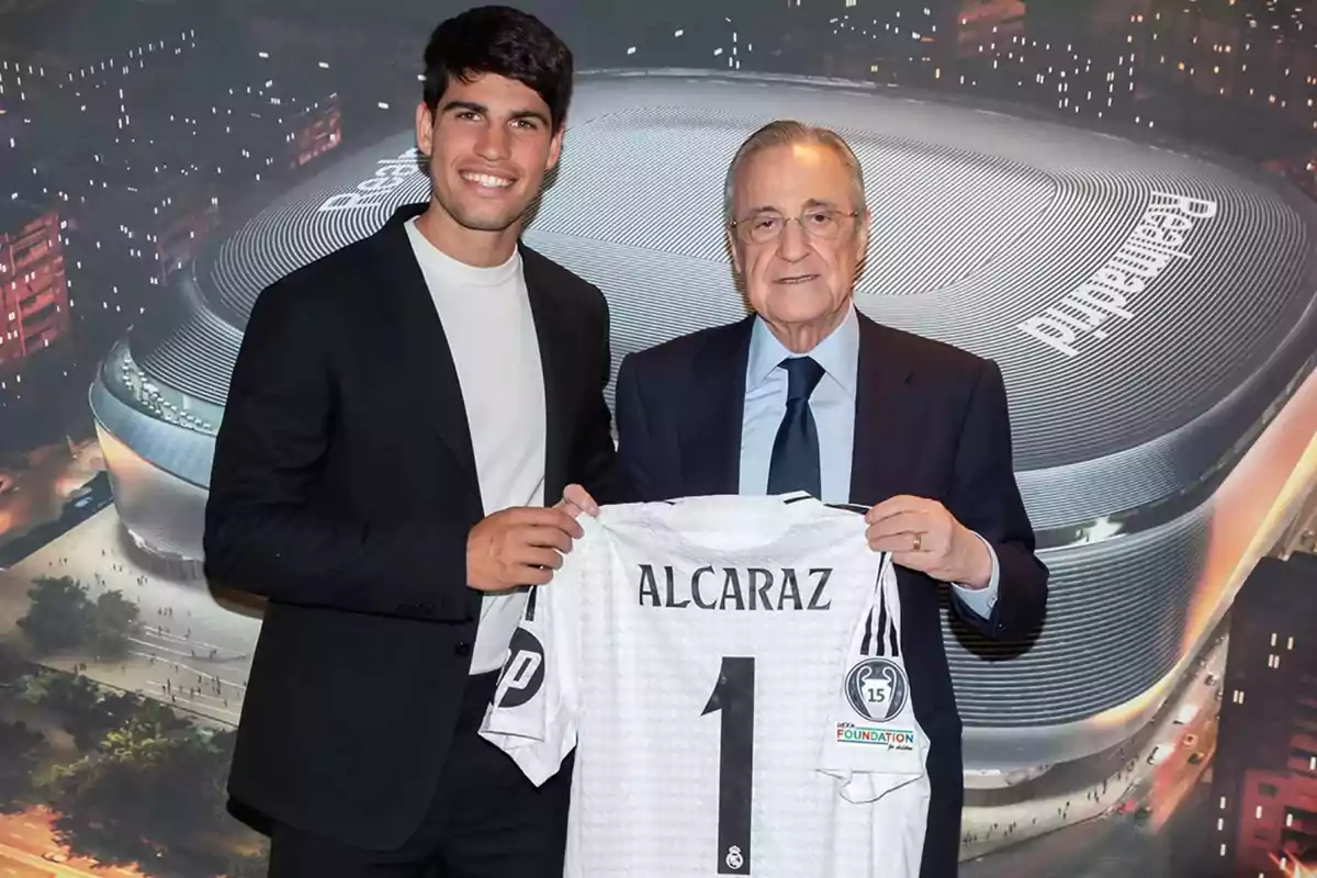 Dos personas posan sonrientes sosteniendo una camiseta blanca con el nombre Alcaraz y el número uno frente a una imagen del estadio Santiago Bernabéu