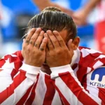 Primer plano de un jugador del Atlético de Madrid con la camiseta rojiblanca cubriéndose la cara con ambas manos en un gesto de profunda frustración tras la derrota ante el Rayo Vallecano.