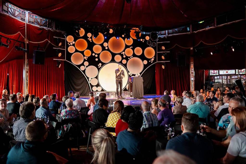 An Idiot's Guide to Wine: espectáculo de comedia donde se ve a un monologuista en el escenario y al público en sus mesas