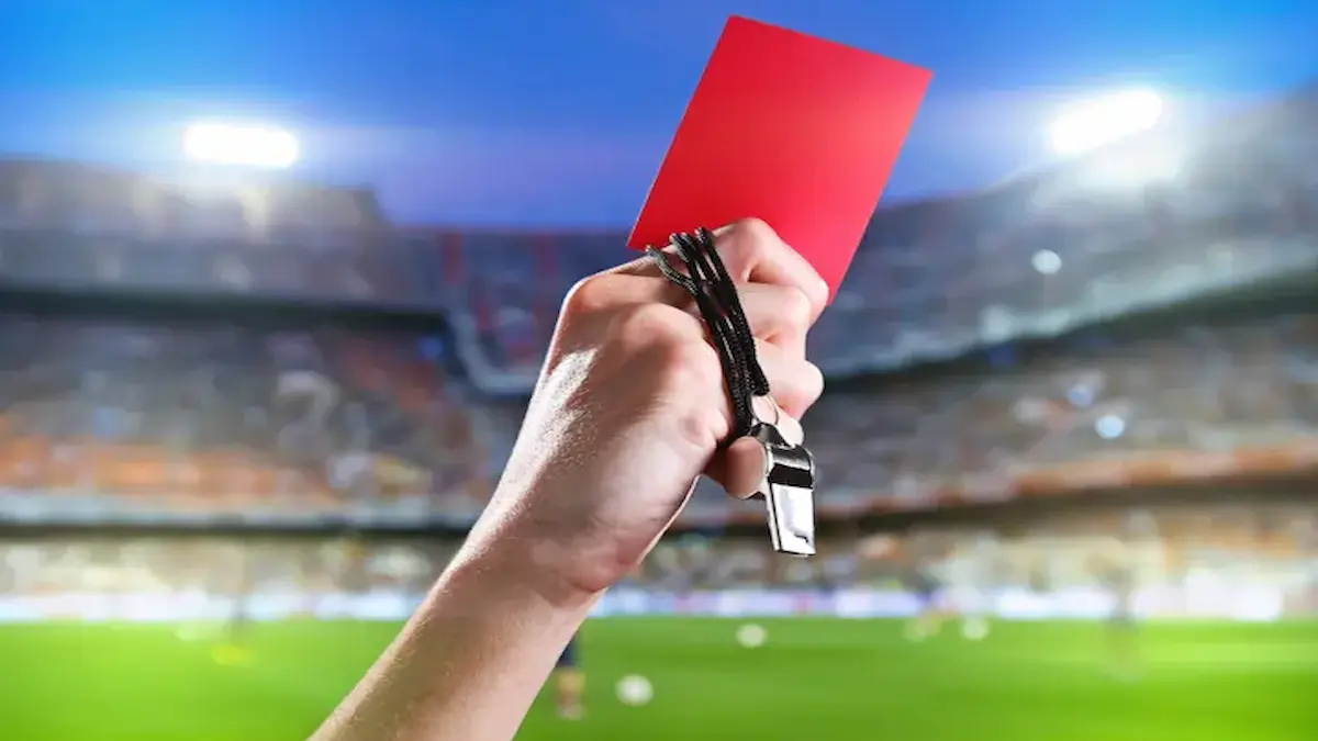 Árbitro de fútbol mostrando una tarjeta roja en un estadio lleno durante un partido de LaLiga.